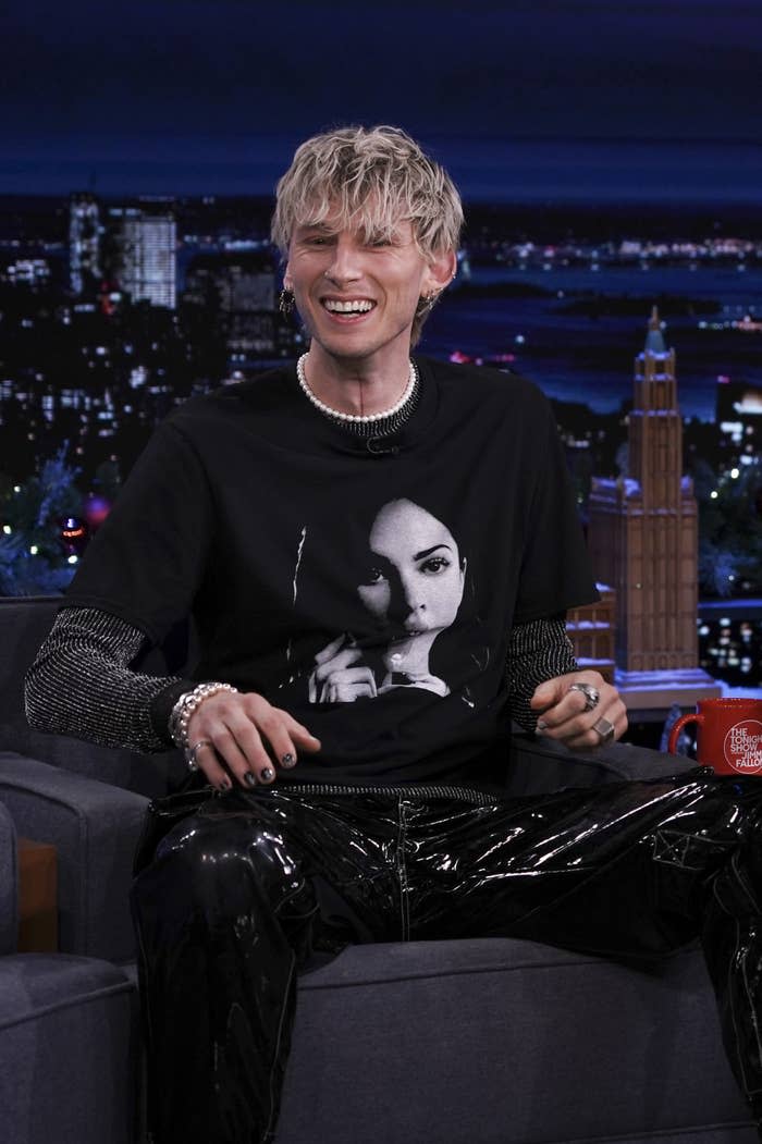 MGK smiling during a late-night TV interview while wearing a t-shirt with Megan's face on it
