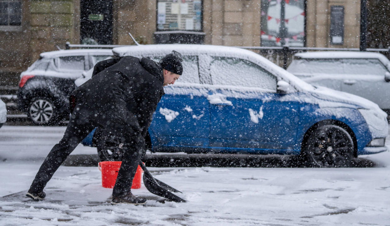 A man clears snow from the pavement in Derbyshire. (SWNS)