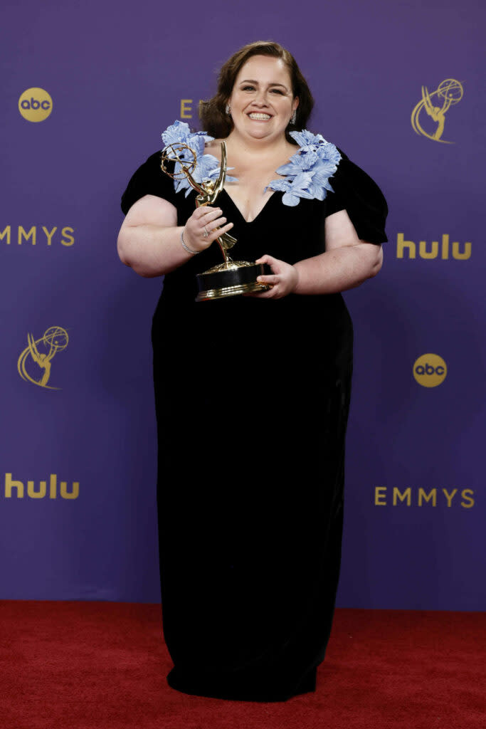 The actor Jessica Gunning on the red carpet wearing a black dress with blue detailing around the neck, holding her Emmy Award