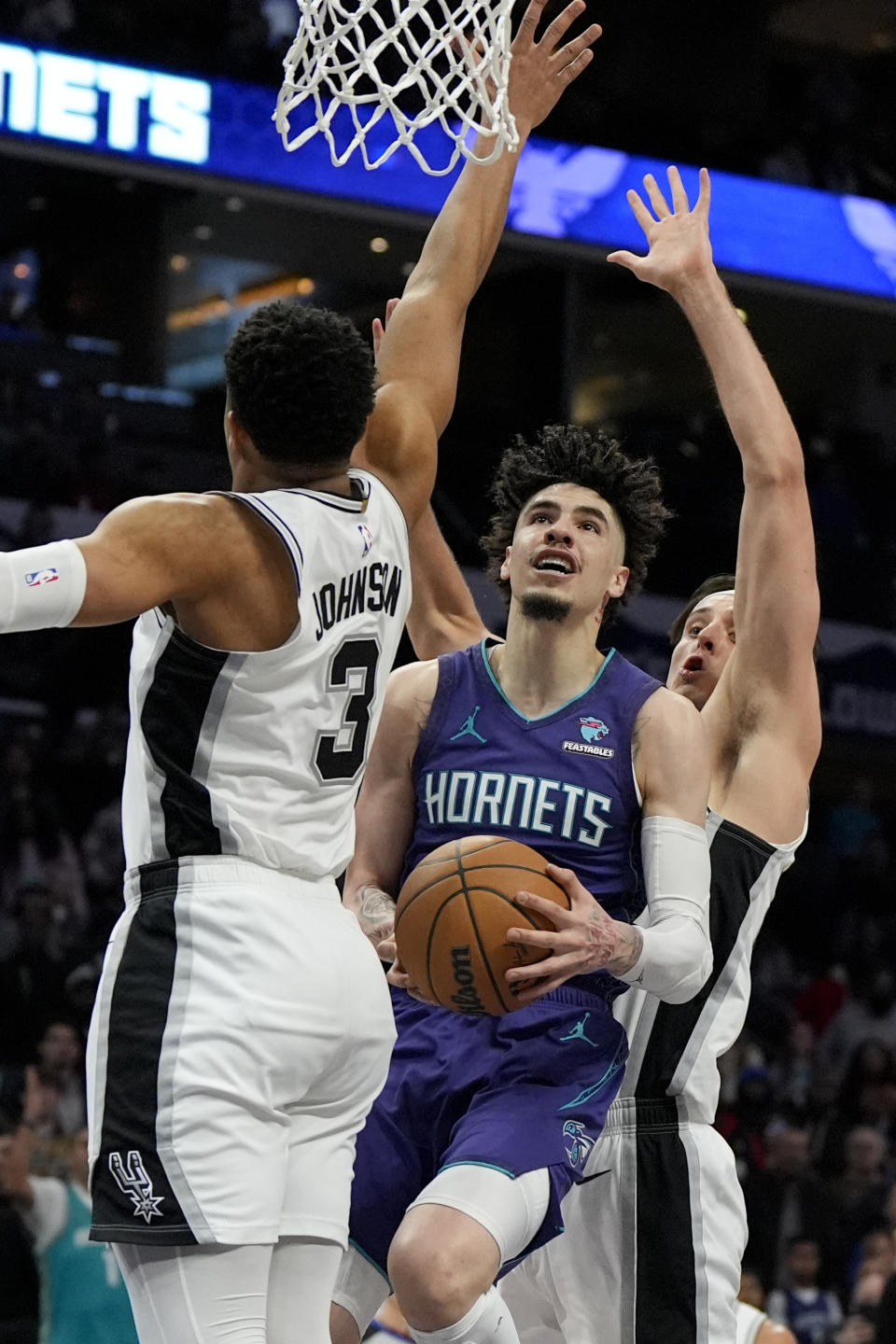 Charlotte Hornets guard LaMelo Ball drives to the basket between San Antonio Spurs forward Zach Collins and forward Keldon Johnson (3) during the second half of an NBA basketball game on Friday, Jan. 19, 2024, in Charlotte, N.C. (AP Photo/Chris Carlson)