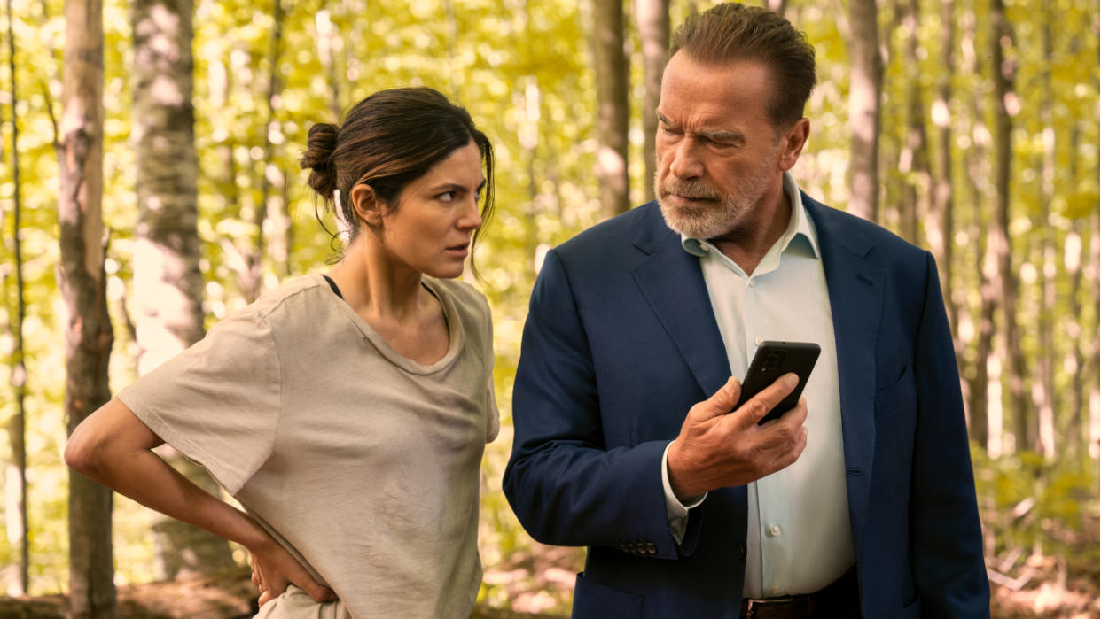  Monica Barbaro and Arnold Schwarzenegger share concern while looking at a phone in the jungle in FUBAR. 