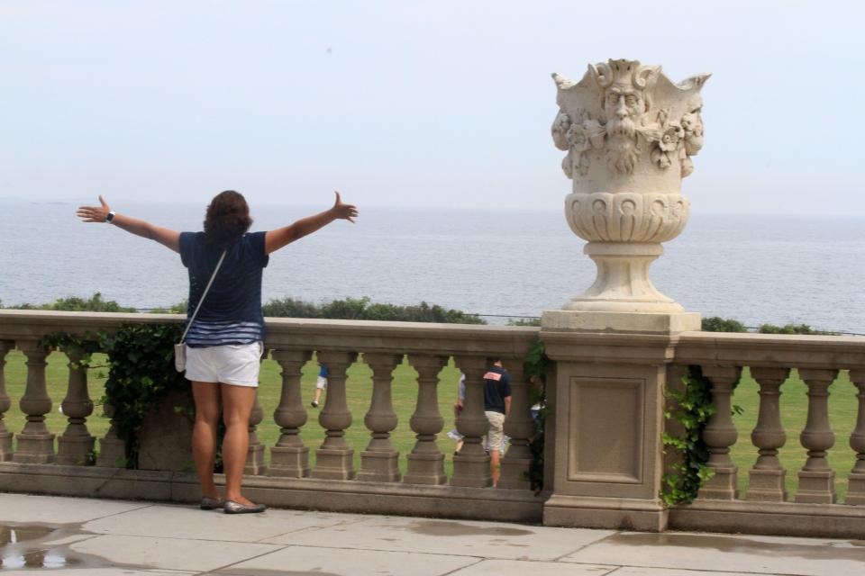 A tourist poses for a picture and takes in the ocean view at The Breakers in Newport.