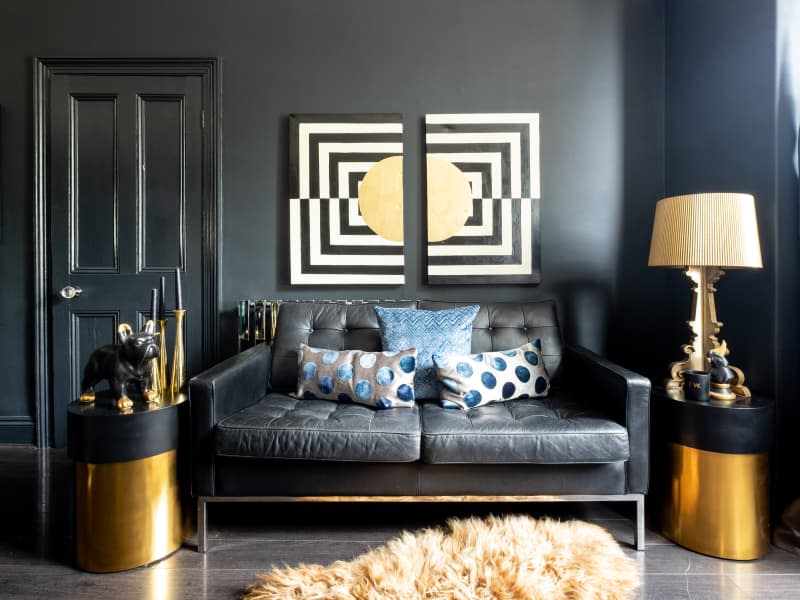 Gold decor, including lamps and furniture accents, near a black couch in a black living room
