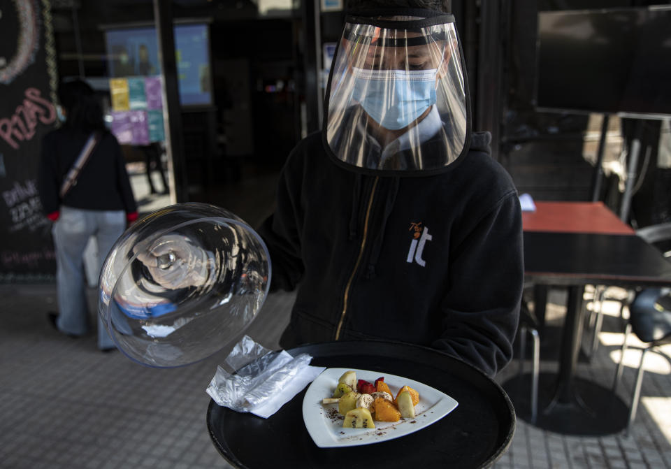 Un mesero, usando equipo de protección, muestra un plato de fruta durante la reapertura de un restaurante en Santiago, Chile, el miércoles 2 de septiembre de 2020. (AP Foto/Esteban Felix)