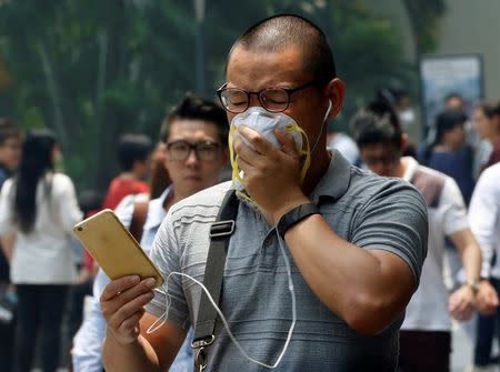 A man covers his face with a mask as haze shrouds Singapore's central business district August 26, 2016. REUTERS/Edgar Su