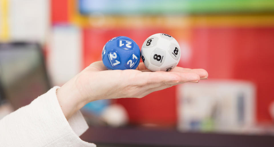 A hand holding up two Powerball balls, 21 and 8.