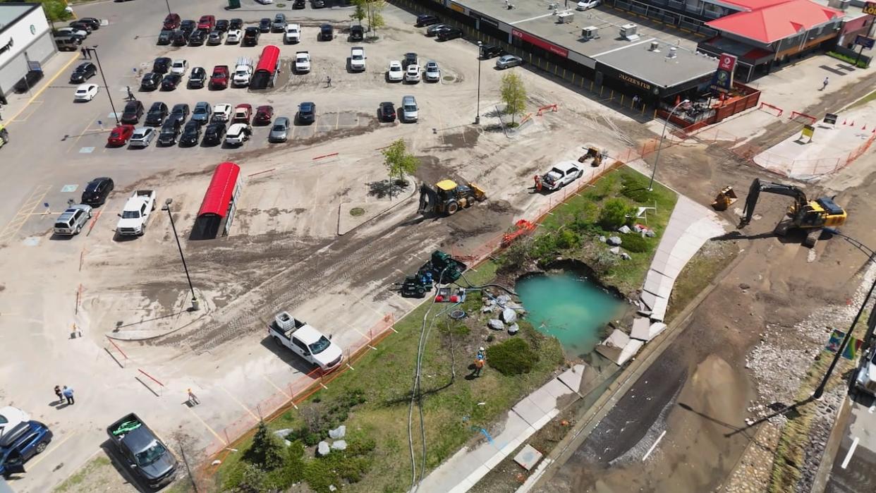 A drone shot of the spot where a catastrophic water main rupture broke ground, next to a plaza on 16 Ave. N.W., just west of Home Road, on June 5. (Monty Kruger/CBC - image credit)