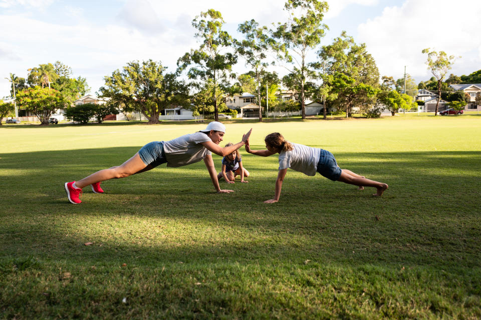 A mother and two daughters exercising in a park.