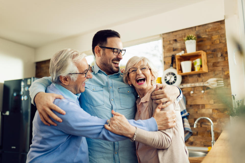 Cheerful mid adult man and his senior parents laughing while embracing in the kitchen.