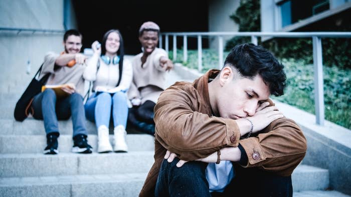 A group of teens points and laughs at a fellow student on campus