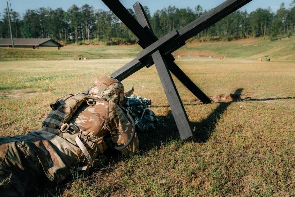 A US Army soldier competing in the Best Ranger Competition aims a rifle while positioned on the ground.