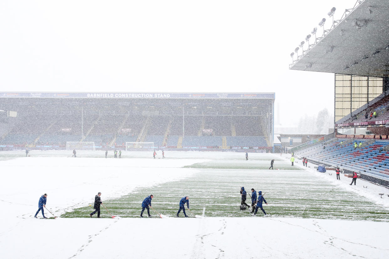 Groundsman attempt to clear snow from the pitch at Turf Moor.