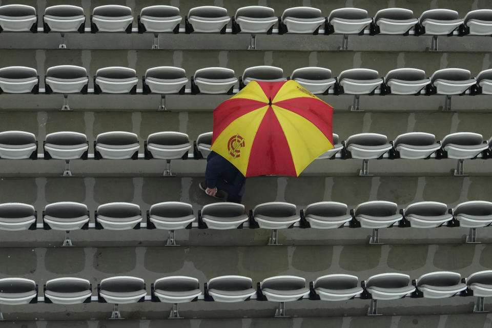 A fan with an umbrella in the colours of the Marylebone Cricket Club (MCC), waits as rain delays the start of play on the third day of the Test match between England and New Zealand at Lord's cricket ground in London, Friday, June 4, 2021. (AP Photo/Kirsty Wigglesworth)