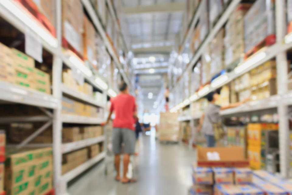 A man pushing a shopping cart down the aisle of a large warehouse store.