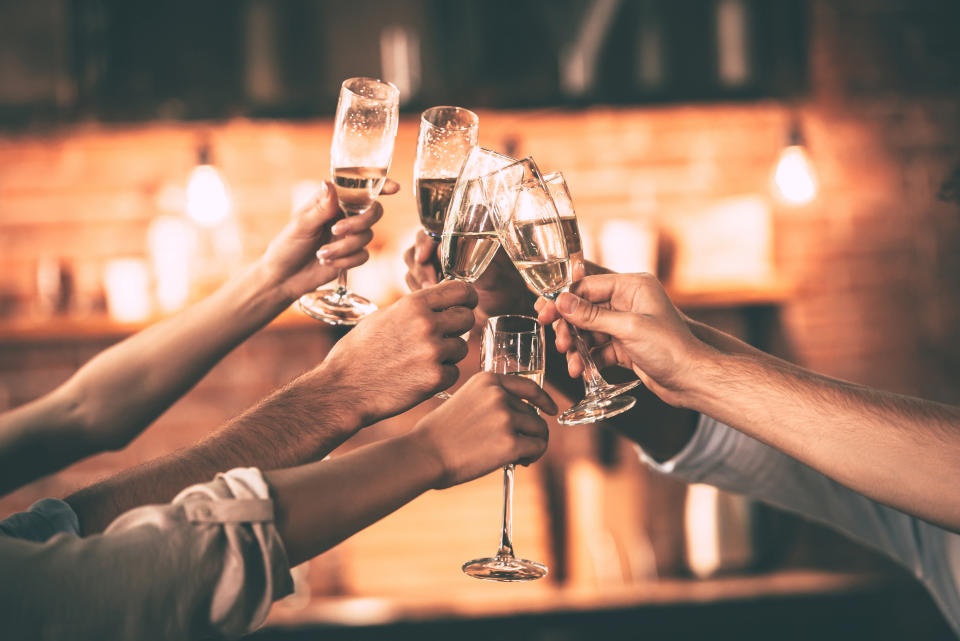 Men and women click their Champagne flutes together in front of a wall