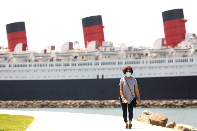 LONG BEACH, CA - MAY 11, 2020 - - Aida Bautista, 75, walks along the pedestrian/bike path against a backdrop of the Queen Mary on the first day that Long Beach reopened the path on Monday May 11, 2020. The city of Long Beach eased a few of its public health restrictions, allowing under certain guidelines the reopening of pedestrian and beach bike paths, tennis centers and courts. Beach bathrooms are also reopening, but the parking lots and beaches still remain closed. (Genaro Molina / Los Angeles Times)