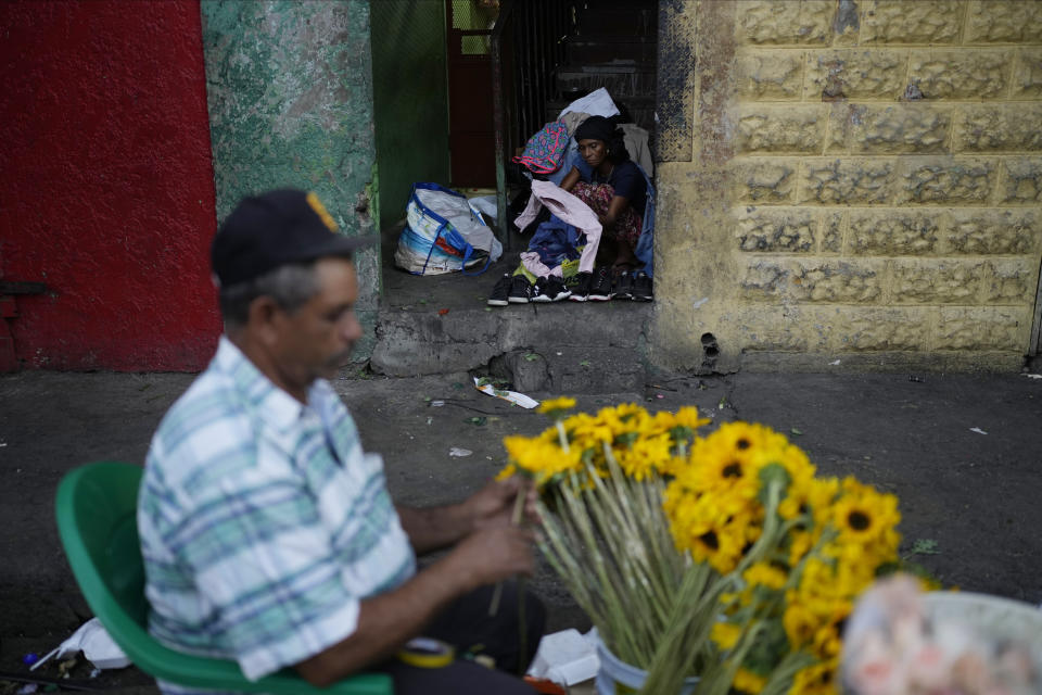 Una persona vende ropa de segunda mano desde la puerta de un edificio mientras un vendedor de flores arregla sus productos en Santo Domingo, República Dominicana, el viernes 24 de marzo de 2023, mientras la nación caribeña da la bienvenida a los invitados a la 28ª Cumbre Iberoamericana. (Foto AP/Ariana Cubillos)