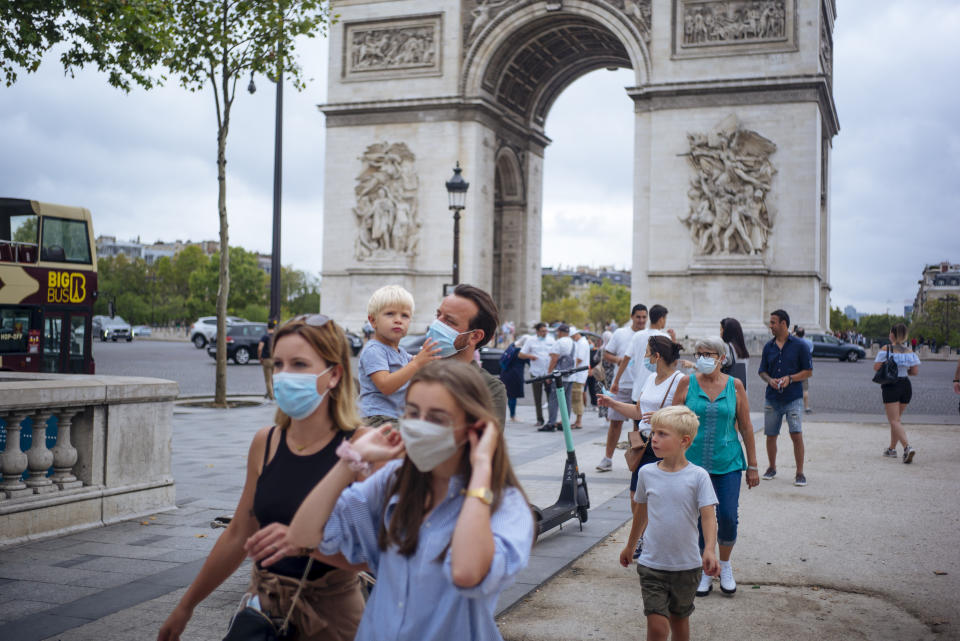 A family wearing protective face masks walk along on the Champs Elysee avenue, with Arc de Triomphe in background, in Paris, Saturday, Aug. 15, 2020. Paris extended the areas of the city where pedestrians will be obliged to wear masks starting Saturday morning after health officials said that the coronavirus is "active". The Champs-Elysees Avenue and the neighbourhood around the Louvre Museum are among zones where masks will be obligatory. (AP Photo/Kamil Zihnioglu)