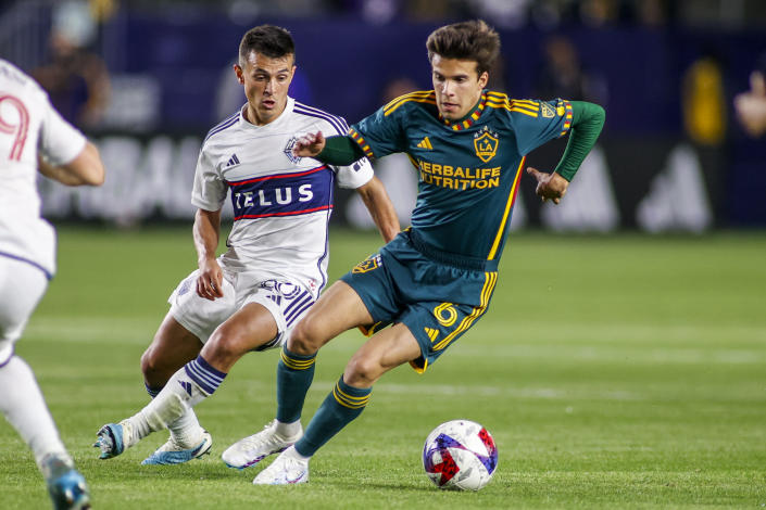 LA Galaxy midfielder Riqui Puig, right, controls the ball away from Vancouver Whitecaps midfielder Andrés Cubas during the second half of an MLS soccer match in Carson, Calif., Saturday, March 18, 2023. (AP Photo/Ringo H.W. Chiu)