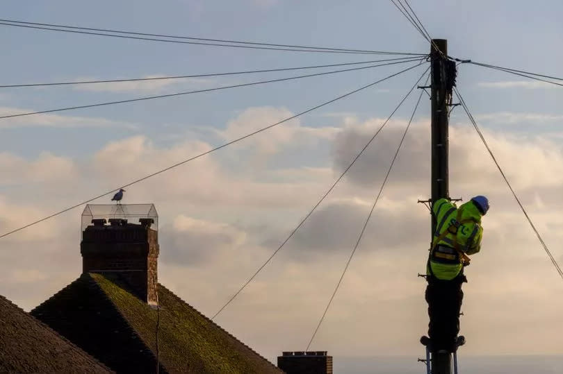 A stock image of a telecommunications engineer working on phone lines half way up a telegraph pole
