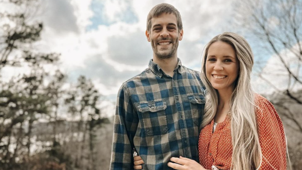 Derick Dillard in a blue plaid shirt smiles with wife Jill Duggar in an orange top