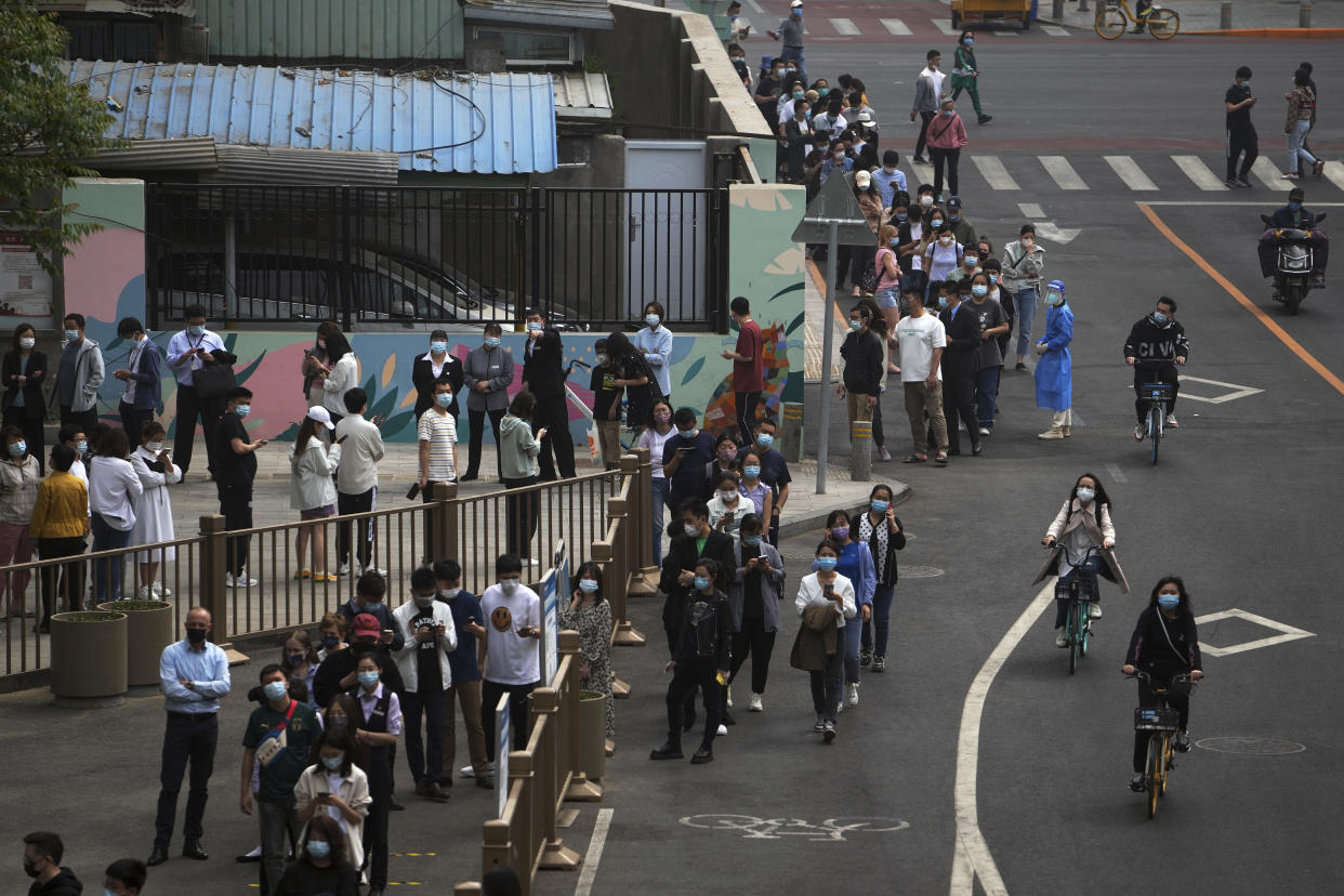 Cyclists pass by residents and office workers who line up on a road for mass coronavirus testing near the residential and commercial office complex at the central business district, Monday, April 25, 2022, in Beijing. (AP Photo/Andy Wong)