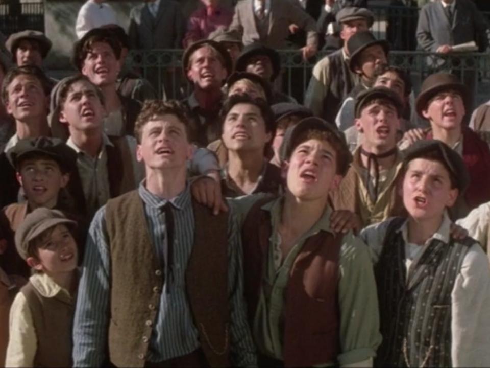 newsies ensemble a bunch of paperboys dressed up and singing in a crowd