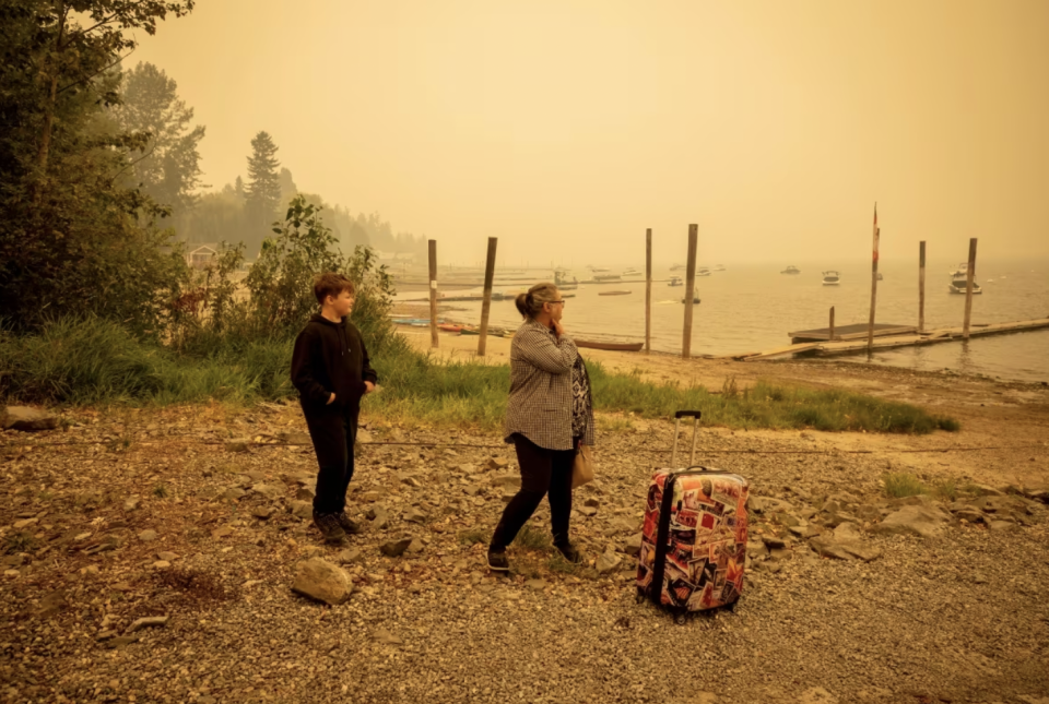 Two people are pictured waiting for a boat ride across Shuswap lake to Celista from Sorrento, B.C., while evacuating from wildfires on Aug. 19. (Ben Nelms/CBC)