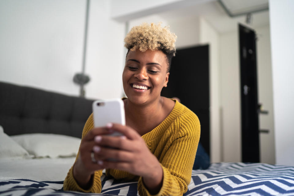 Young woman lying on bed and using smartphone