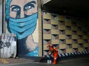 FILE PHOTO: A worker wearing a protective face mask sweeps the street near a mural promoting awareness of the coronavirus disease (COVID-19) outbreak in Jakarta