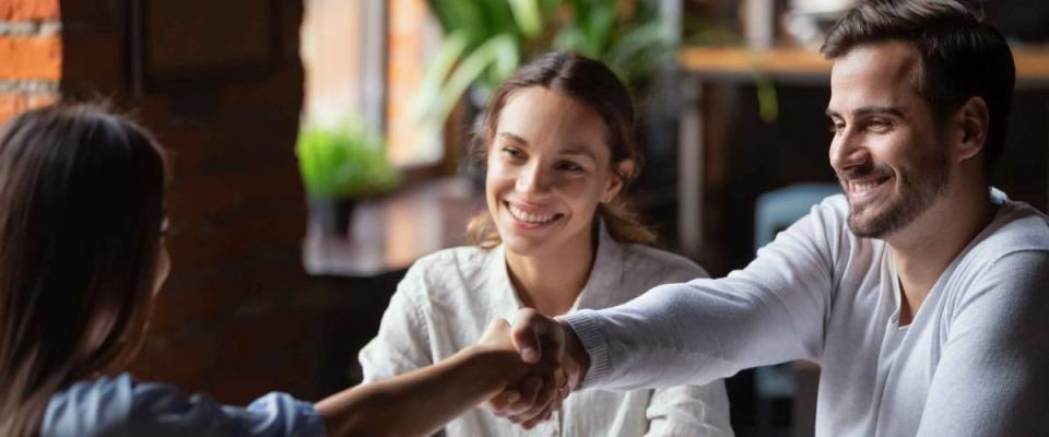 Smiling couple shaking hands with person across the table in an office setting.