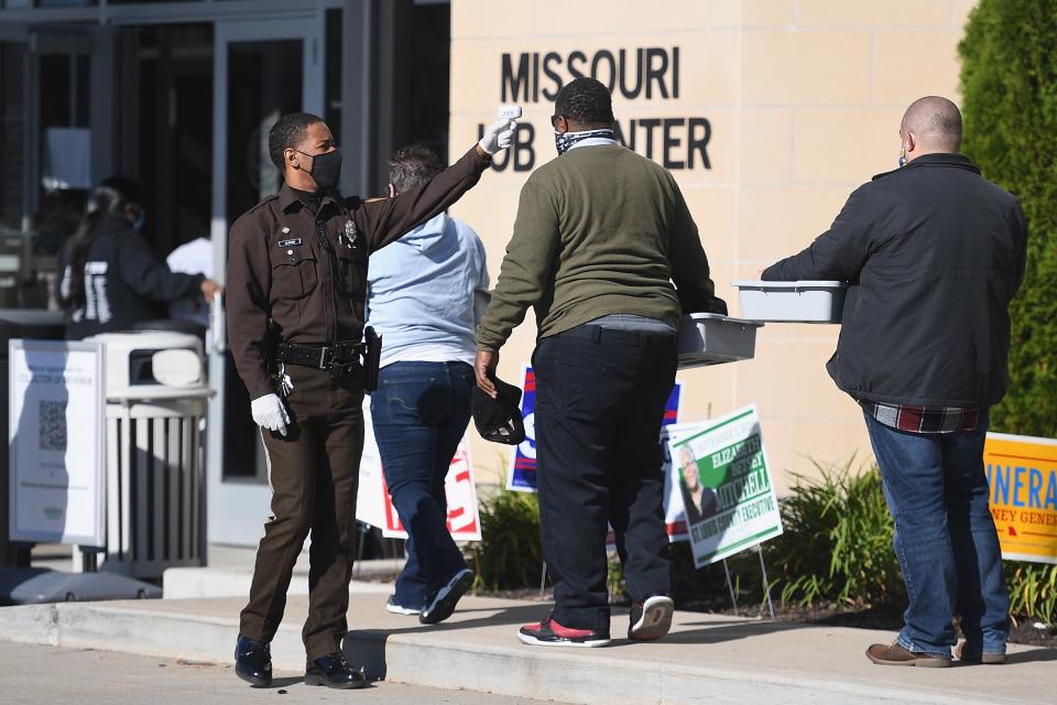 A law enforcement officer screens voters' temperatures as they wait in line to cast their ballots in St. Ann, Missouri, November 3, 2020.