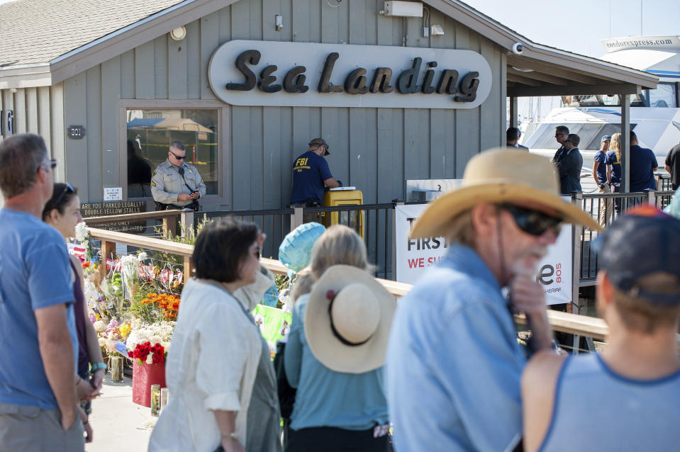 A crowd gathers around a memorial for the victims of the Conception dive boat as FBI's Evidence Response Team agents and other agencies search the Truth Aquatics' offices, the California company that owned the scuba diving boat that caught fire and killed 34 people last week, as authorities issue a search warrant for the company and the sister vessels of the Conception dive boat on the Santa Barbara Harbor in Santa Barbara, Calif., Sunday, Sept. 8, 2019. The office was ringed in red "crime scene" tape as more than a dozen agents took photos and carried out boxes. (AP Photo/Christian Monterrosa)