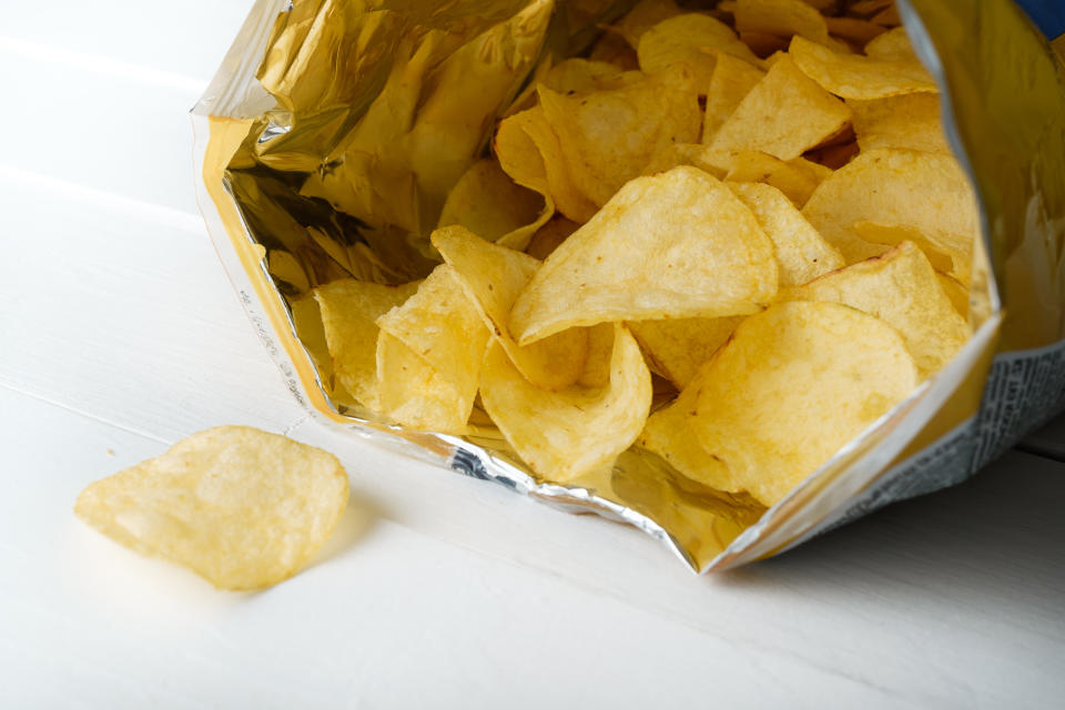 Open bag of potato chips with a few chips spilling out on a white surface