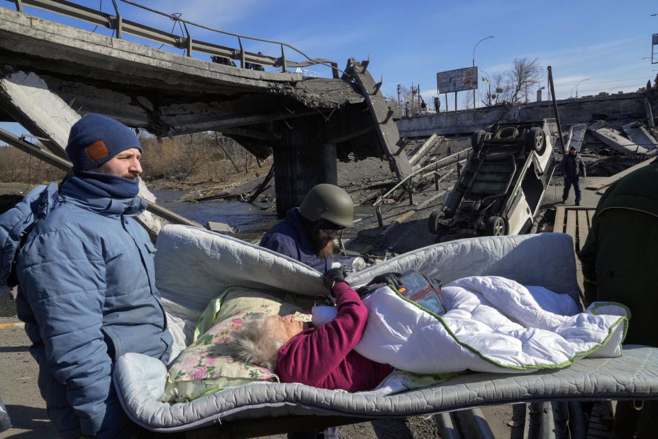 Volunteers pass an improvised path under a destroyed bridge as they evacuate an elderly resident in Irpin, some 25 km (16 miles) northwest of Kyiv, Friday, March 11, 2022. Kyiv northwest suburbs such as Irpin and Bucha have been enduring Russian shellfire and bombardments for over a week prompting residents to leave their home. (AP Photo/Efrem Lukatsky)