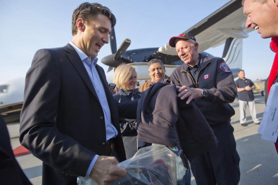 Prime Minister Justin Trudeau is presented with a jacket from Fort McMurray fire chief Darby Allen in Edmonton, Friday, May 13, 2016, before a flight to Fort McMurray. Trudeau is making the visit to see first-hand the devastation caused by the wildfire that forced the evacuation of the city. THE CANADIAN PRESS/Jason Franson