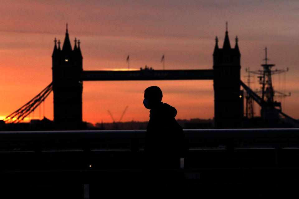 A person wearing a face mask to try to stop the spread of coronavirus walks across London Bridge, with Tower Bridge in the background, at sunrise in London, Monday, Oct. 12, 2020. In response to the coronavirus' resurgence, British Prime Minister Boris Johnson is expected to announce in Parliament on Monday a three-tier local lockdown system, formally known as "Local COVID Alert Levels," for England, his office said. (AP Photo/Matt Dunham)