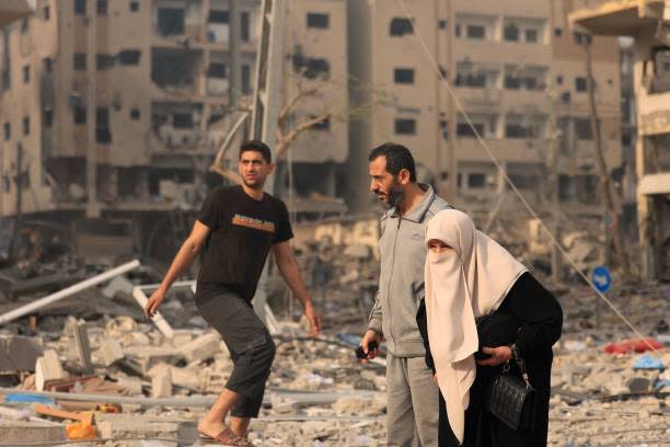 Palestinians walk through a ravaged neighbourhood as they move to safer areas following Israeli airstrikes on Gaza City on Tuesday (AFP via Getty Images)