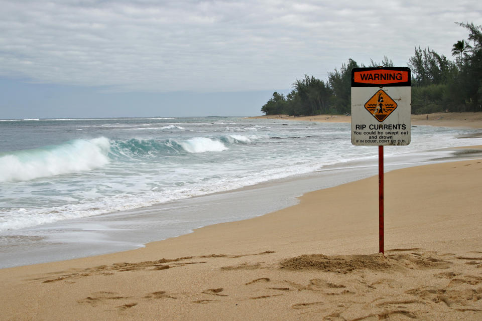 A beach scene with a "Warning: Rip currents" sign in the sand