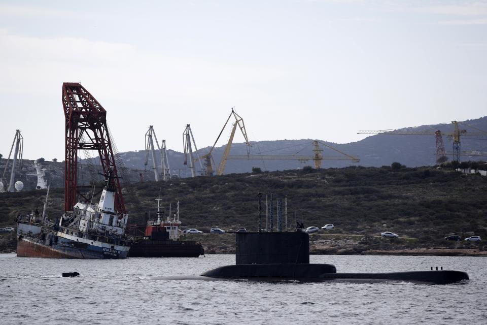 A submarine approaches its naval base as a half sunken ship is seen near a shipyard on Salamina island, west of Athens, on Tuesday, Feb. 12, 2020. Greece this year is commemorating one of the greatest naval battles in ancient history at Salamis, where the invading Persian navy suffered a heavy defeat 2,500 years ago. But before the celebrations can start in earnest, authorities and private donors are leaning into a massive decluttering operation. They are clearing the coastline of dozens of sunken and partially sunken cargo ships, sailboats and other abandoned vessels. (AP Photo/Thanassis Stavrakis)