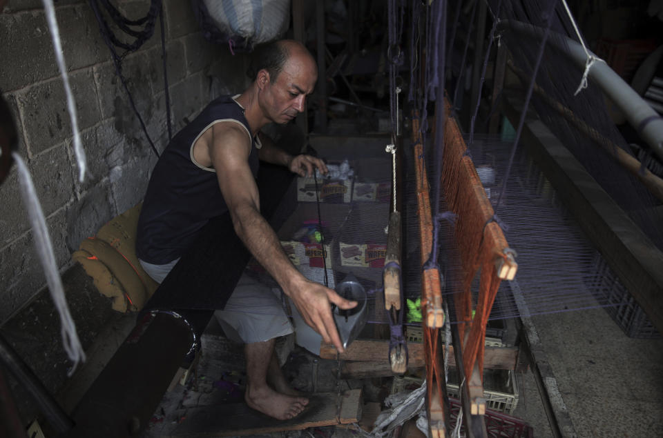 In this Saturday, July 6, 2019 photo, a Palestinian worker weaves carpets on a traditional wooden loom at a carpets factory in Gaza City. Talk about old Gaza, and what pops up are images of clay pottery, colorful glassware, bamboo furniture and ancient frame looms weaving bright rugs and mats. As such professions could be dying worldwide, the pace of their declining is too fast in Gaza that out of its some 500 looms, only one is still functioning. (AP Photo/Khalil Hamra)