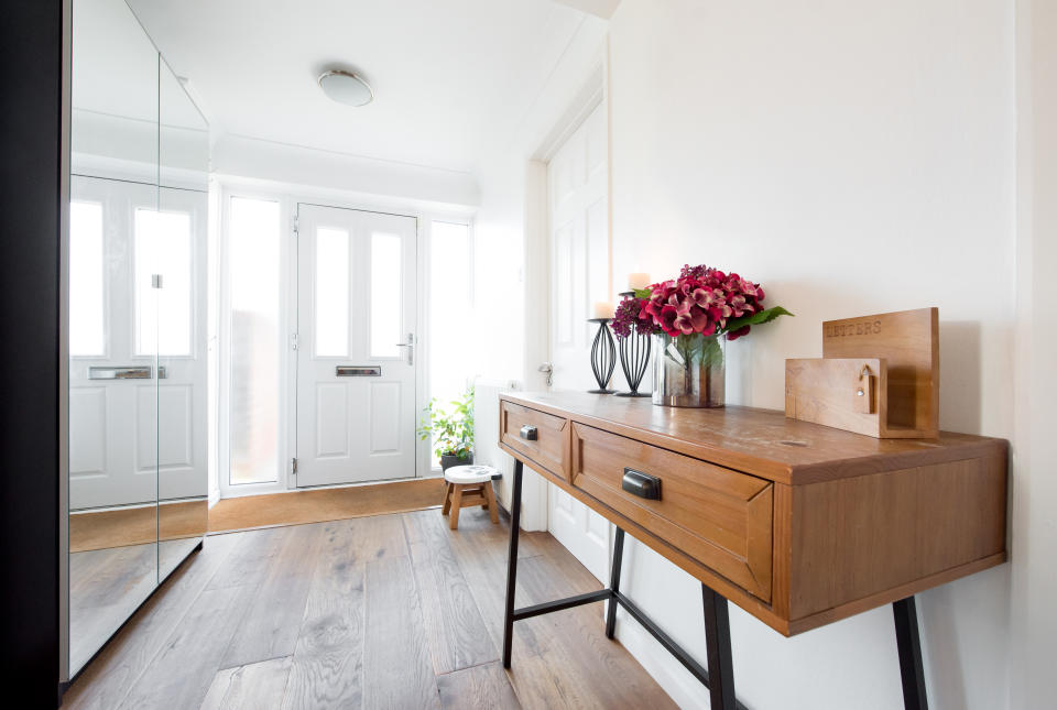 A wooden hall console table with metal legs, vase with flowers, two metal wire candle holders with burning candles