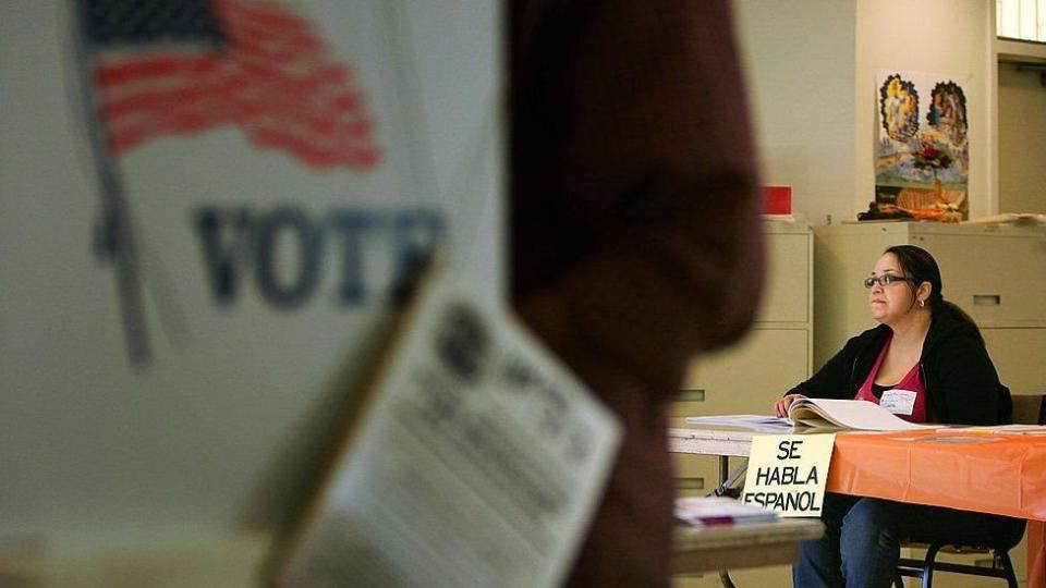Un centro de votación en Estados Unidos en el que una mujer está sentada en una mesa de la que cuelga un aviso que dice "Se habla español".