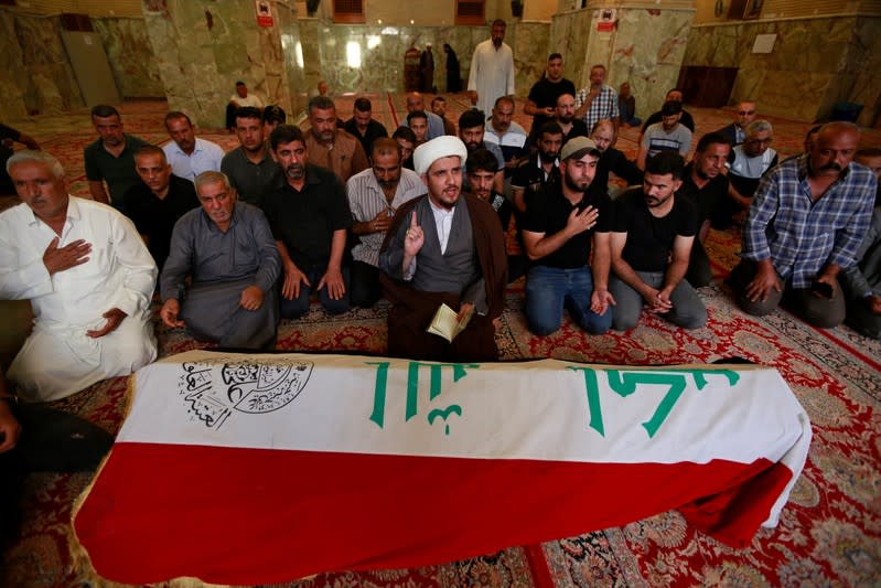 Mourners sit next to the coffin of a demonstrator who was killed at anti-government protests, during a funeral in a mosque in Najaf