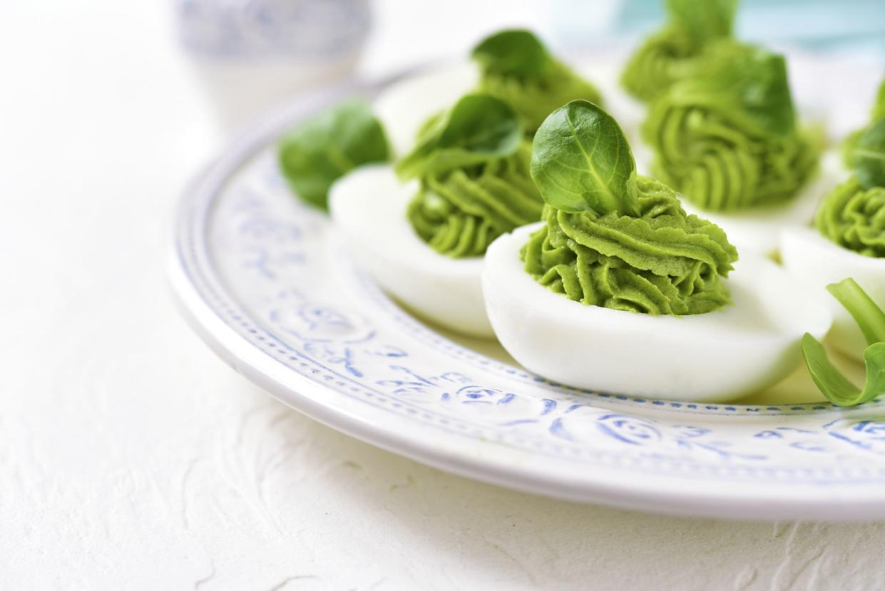 Eggs stuffed with avocado and spinach on a vintage plate on a light background.
