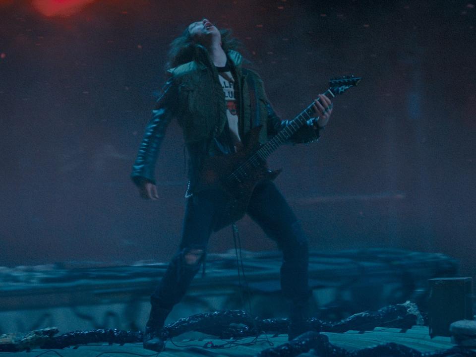 eddie munson playing guitar in stranger things, standing on top of a roof in the upside down and throwing his head back