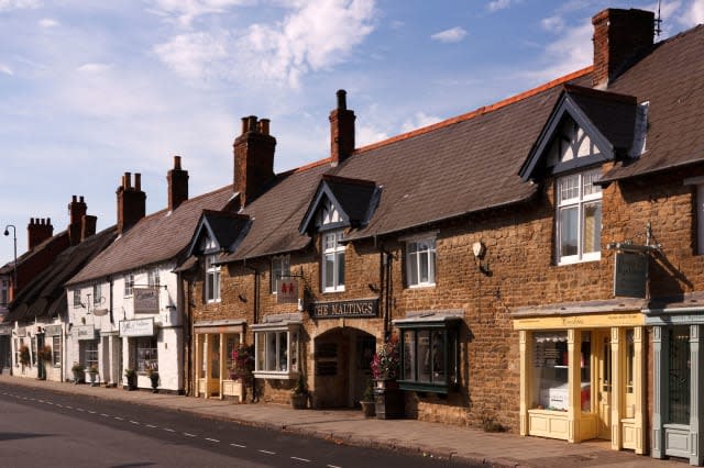 A row of traditional old shop fronts, signs and along town centre shopping street, Mill street, Oakham, Rutland, England, UK