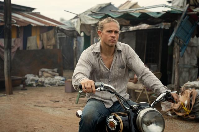 Still from Shantaram. Blond man rides a motorcycle through poor neighbourhoods of India