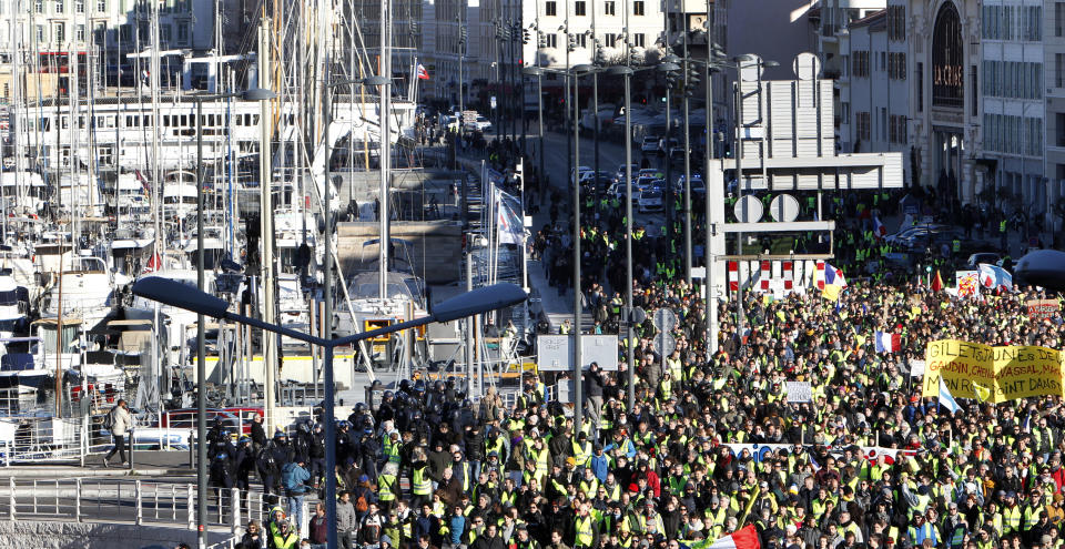 Yellow vest protesters pass through the old harbor as they demonstrate in Marseille, southern France, Saturday, Jan. 12, 2019. Paris brought in armored vehicles and the central French city of Bourges shuttered shops to brace for new yellow vest protests. The movement is seeking new arenas and new momentum for its weekly demonstrations. Authorities deployed 80,000 security forces nationwide for a ninth straight weekend of anti-government protests. (AP Photo/Claude Paris)