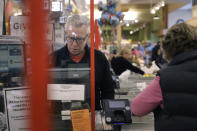 Cashier George Wallace, of Quincy, Mass., center, works while standing behind a plastic shield Thursday, March 26, 2020, at the checkout in a grocery store, in Quincy, Mass. Grocery stores across the U.S. are installing protective plastic shields at checkouts to help keep cashiers and shoppers from infecting each other with the coronavirus. The new coronavirus causes mild or moderate symptoms for most people, but for some, especially older adults and people with existing health problems, it can cause more severe illness or death. (AP Photo/Steven Senne)